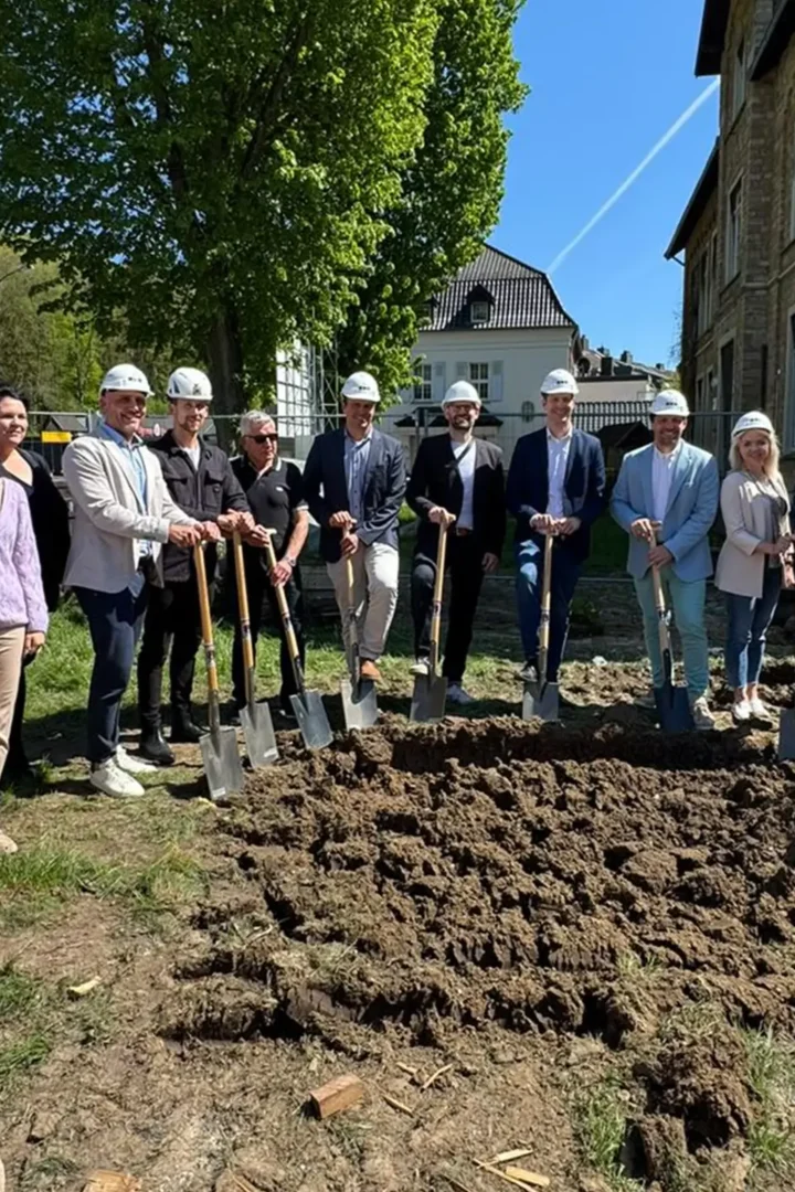 Personen stehen mit Spaten an aufgelockerter Erde