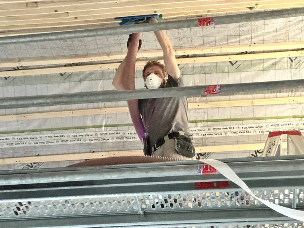 Handwerker beim Wiederaufbau eines Dachstuhls in Stolberg, arbeitet mit Atemschutzmaske an der Holzdecke im Rohbau.