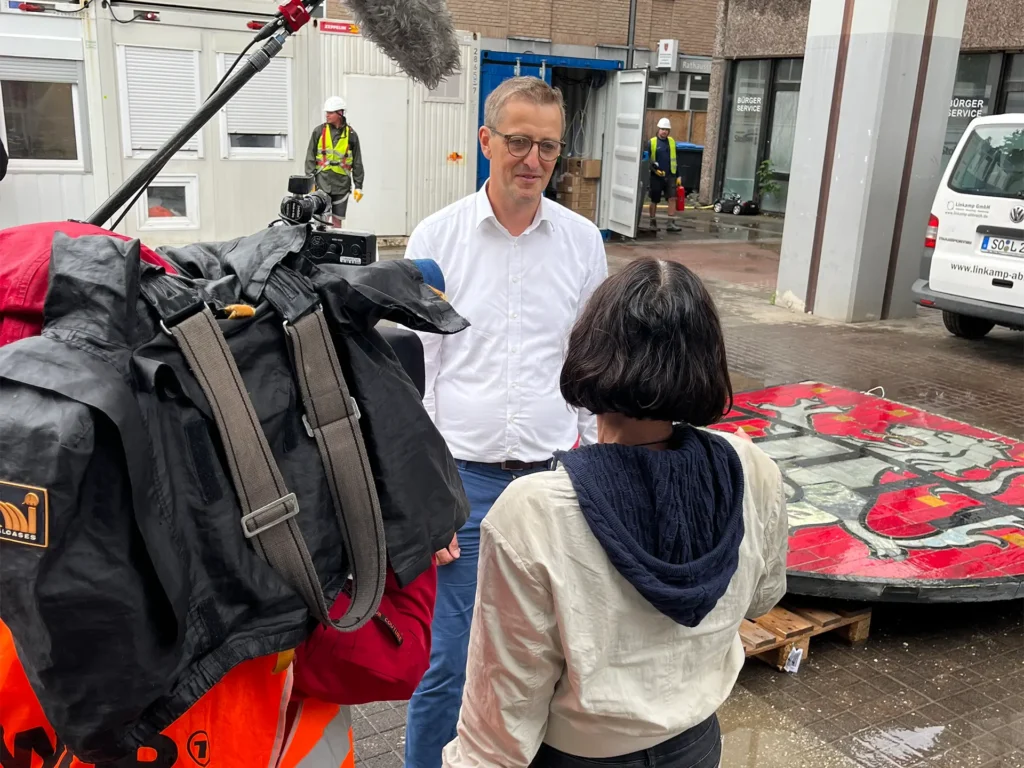 Wilfried Sterck spricht mit einer Reporterin vor dem Stadtwappen