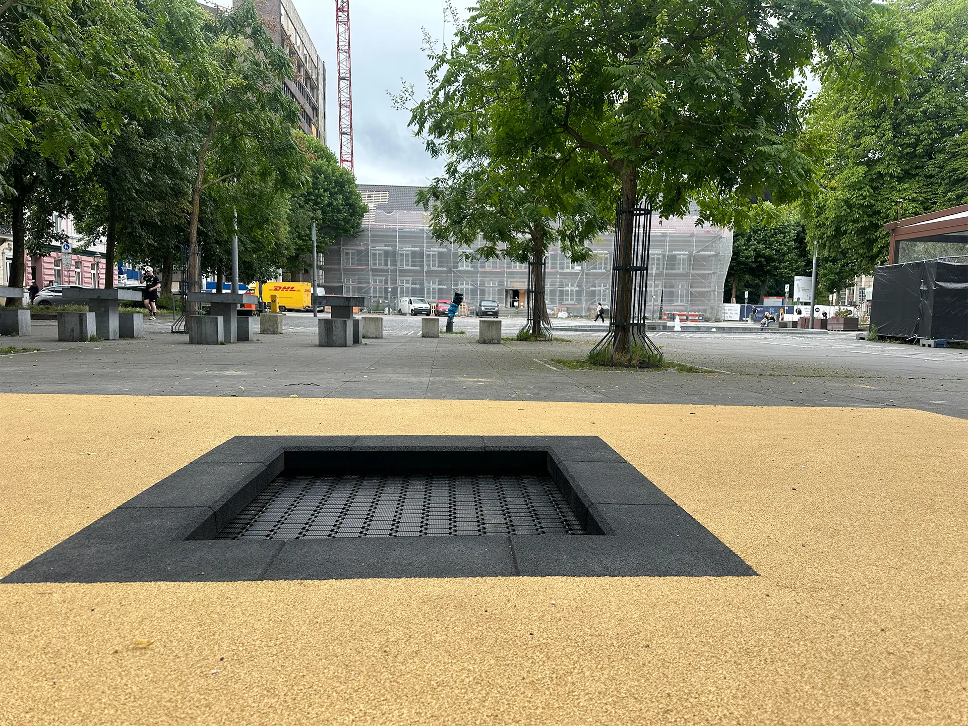 Barrierefreier Platz mit zwei eingebauten Bodentrampolinen auf hellem Fallschutzbelag in der Innenstadt von Stolberg, NRW – Teil des Wiederaufbaus nach dem Hochwasser 2021, um urbanen Raum familienfreundlich zu gestalten.
