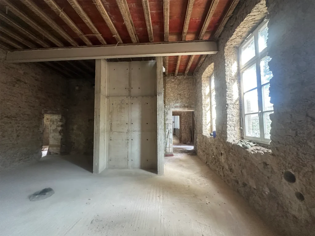 Rohbau mit freigelegten Natursteinwänden, neu eingebauten Betonstützen und großen Fenstern für mehr Stabilität und Licht