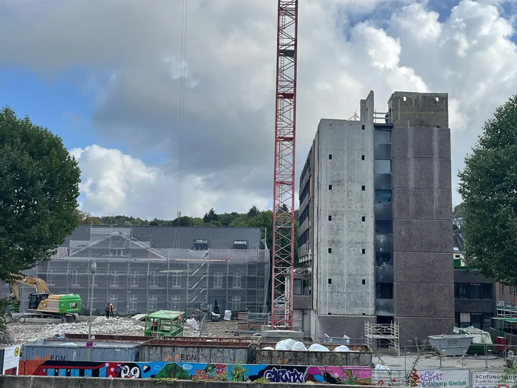 Teilweise abgerissenes Verwaltungsgebäude in Stolberg mit freigelegter Fassade, Baukran und Bagger im Einsatz, davor Arbeiter auf der Baustelle.