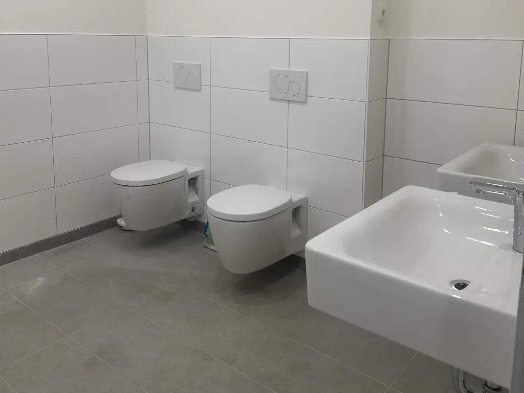 moderne Sanitärräume mit neuen Fliesen, Hänge-WCs und Waschbecken im Baufortschritt