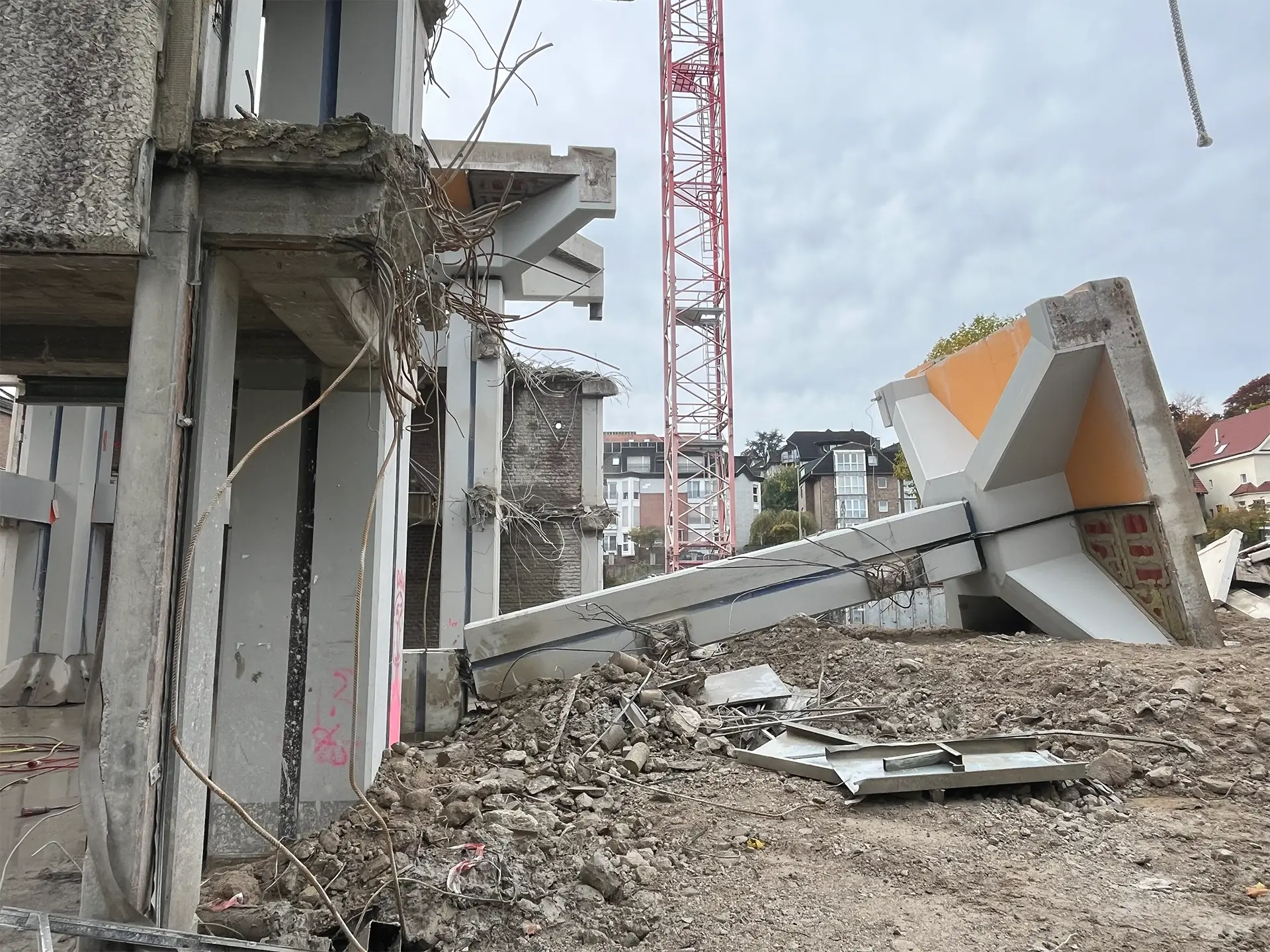 Teilweise abgerissenes Betongebäude mit freiliegenden Stahlarmierungen, umgeben von Schutt und Trümmern. Im Hintergrund ist ein roter Baukran zu sehen.