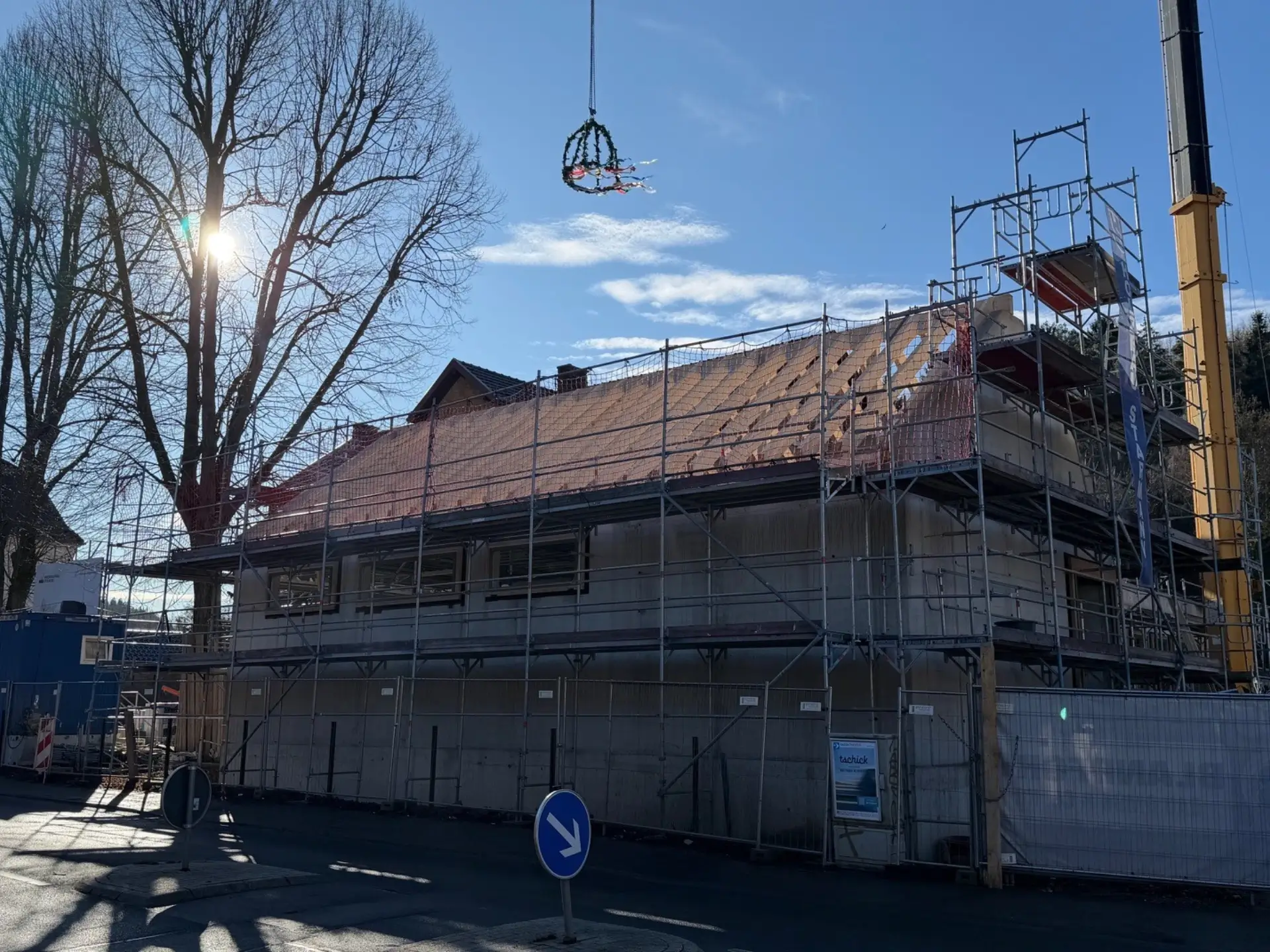 Weitaufnahme einer Baustelle mit eingerüstetem Gebäude, Baukran und schwebendem Richtkranz über dem Dach.