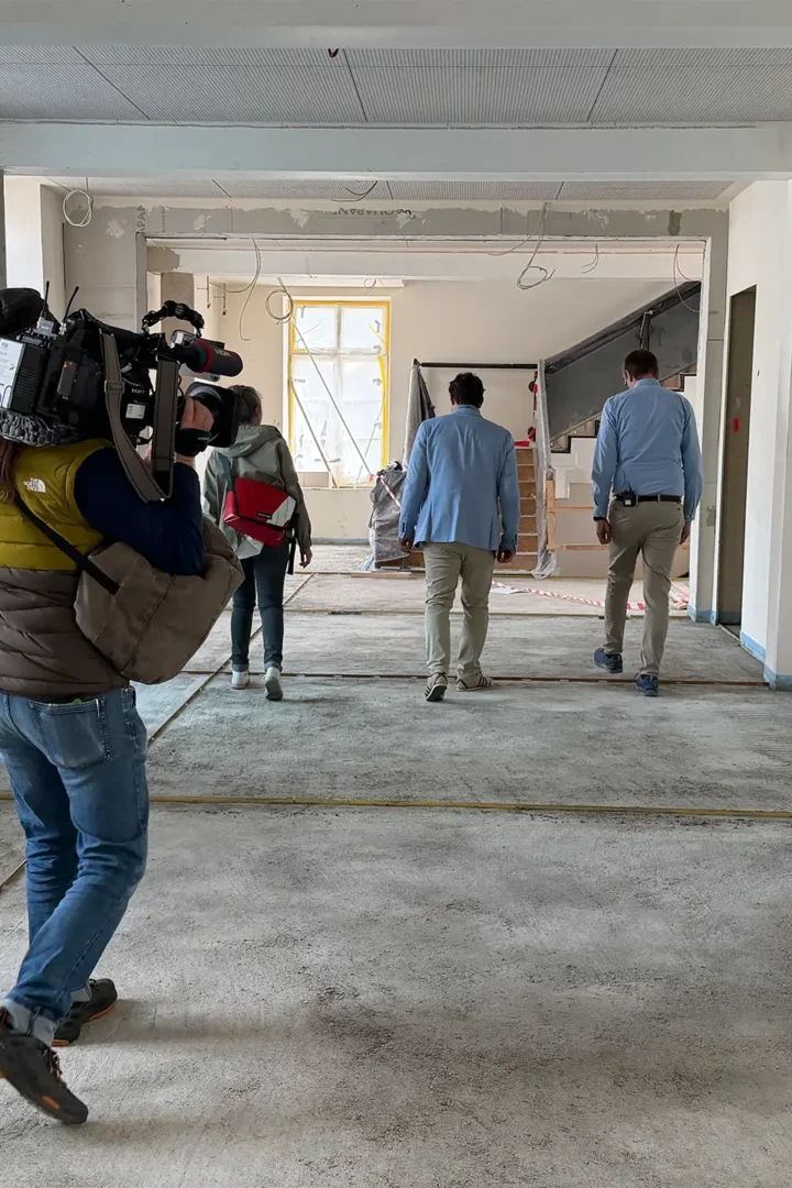 Personengruppe läuft durch einen im Umbau befindlichen Innenraum, begleitet von einem Kamerateam