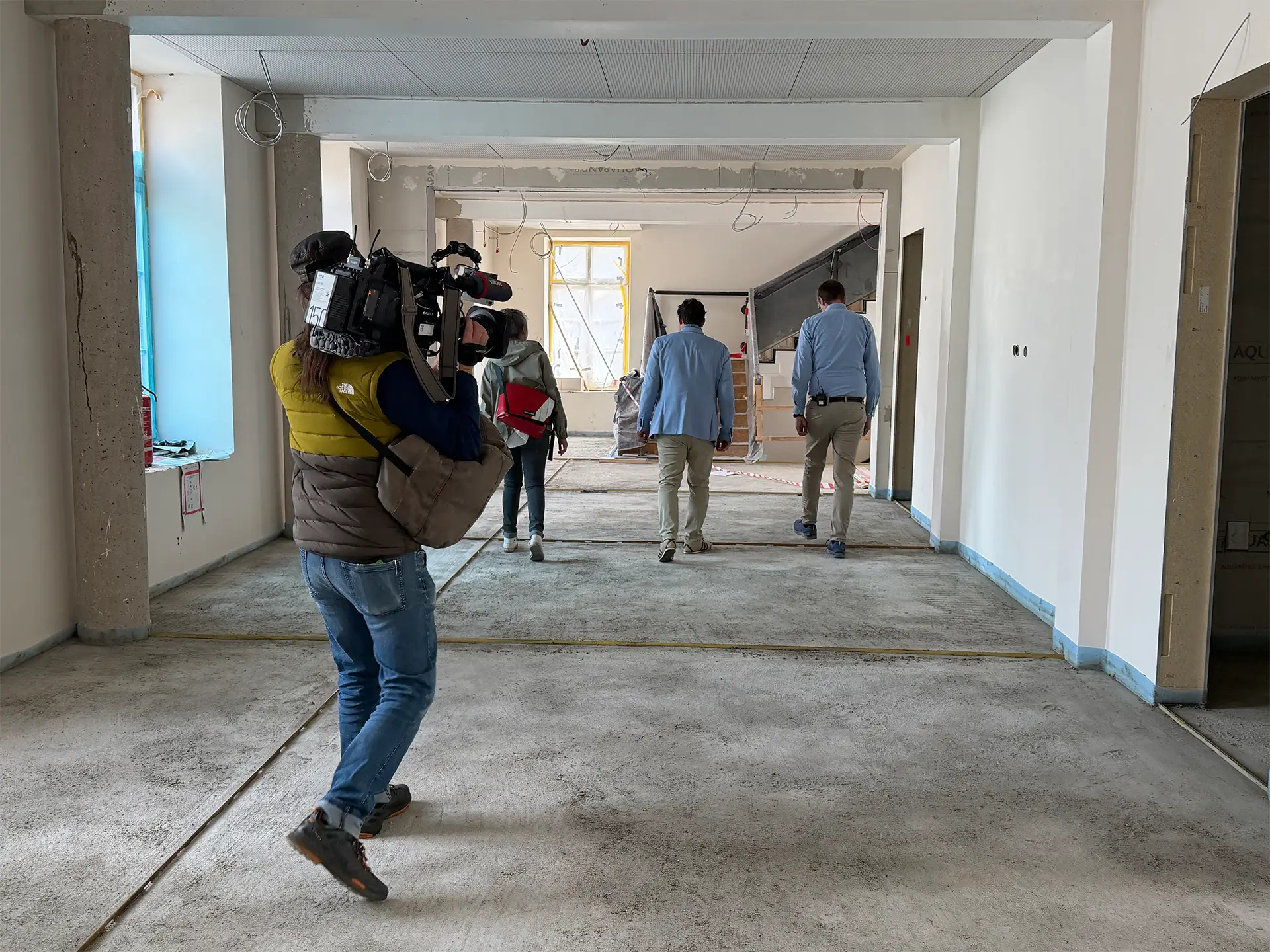 Personengruppe läuft durch einen im Umbau befindlichen Innenraum, begleitet von einem Kamerateam