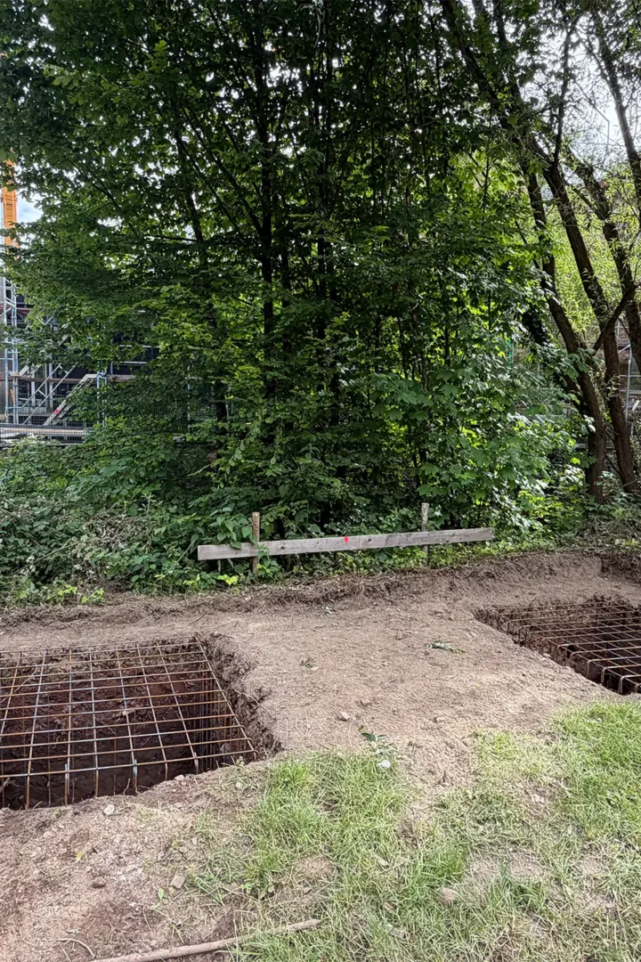 Ausgehobene Fundamentgruben mit Bewehrungsstahl auf dem Gelände des Wiederaufbauprojekts. Die vorbereiteten Fundamente bilden die Grundlage für den nächsten Bauabschnitt des Anbaus.