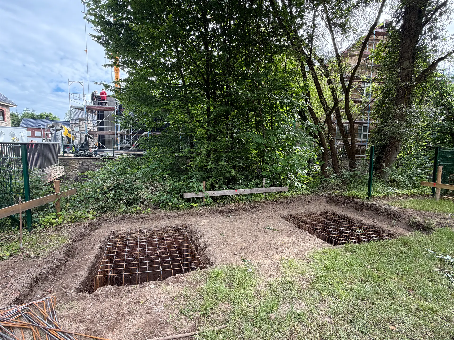 Ausgehobene Fundamentgruben mit Bewehrungsstahl auf dem Gelände des Wiederaufbauprojekts. Die vorbereiteten Fundamente bilden die Grundlage für den nächsten Bauabschnitt des Anbaus.