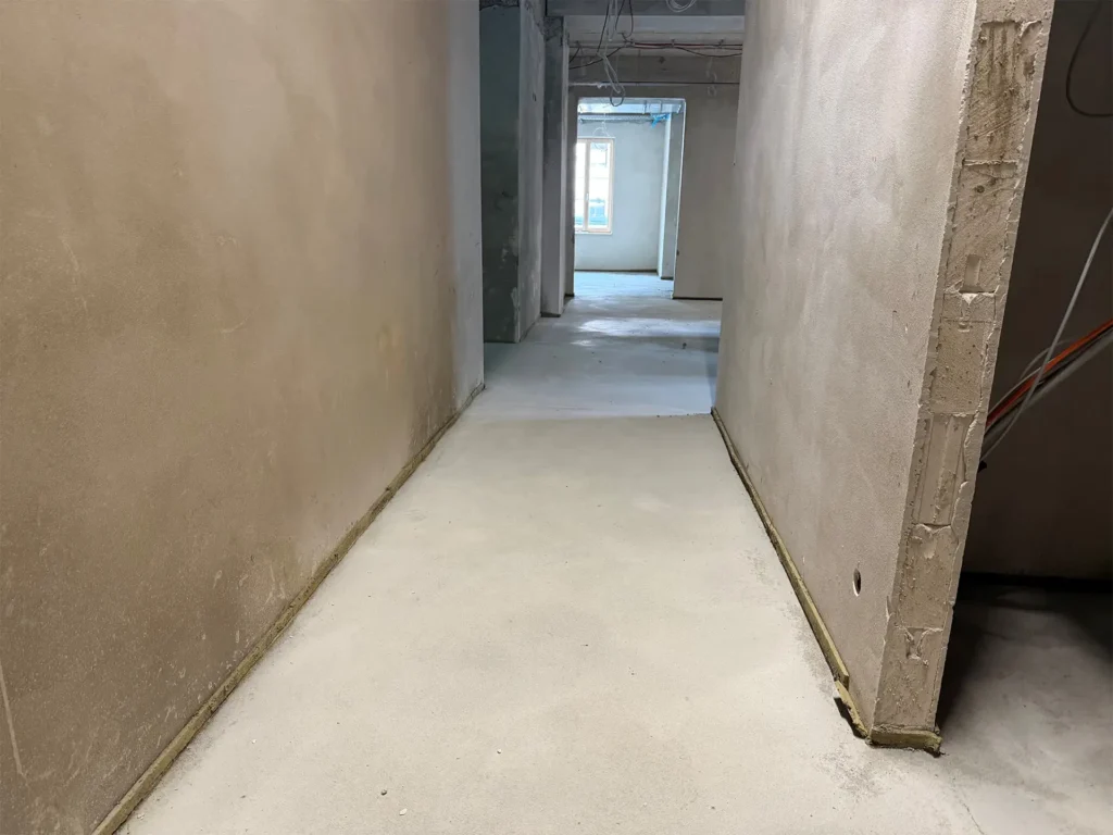 Flurbereich im Innenausbau des neuen Rathauses in Stolberg mit verputzten Wänden, fertigem Estrich und vorbereiteten Installationen. Der Blick führt durch den Flur in weitere entstehende Büroräume.
