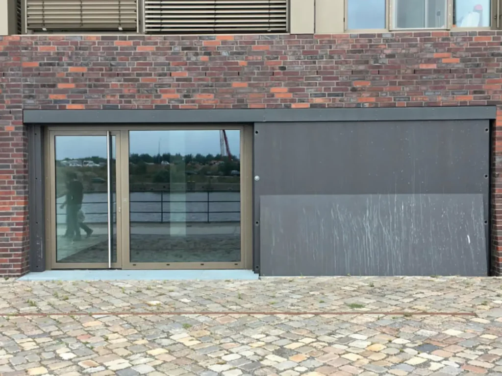 Hochwasserschutz am neuen Rathaus Stolberg mit mobiler Schutzwand vor einem Gebäudeeingang als Teil des nachhaltigen Sicherheitskonzepts.