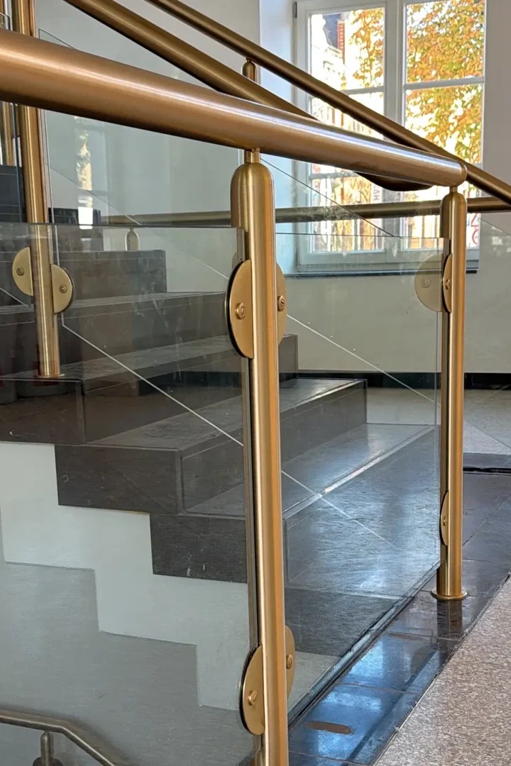 Modernisiertes Treppenhaus im historischen Rathaus Stolberg mit Glasgeländer und goldfarbenen Handläufen.