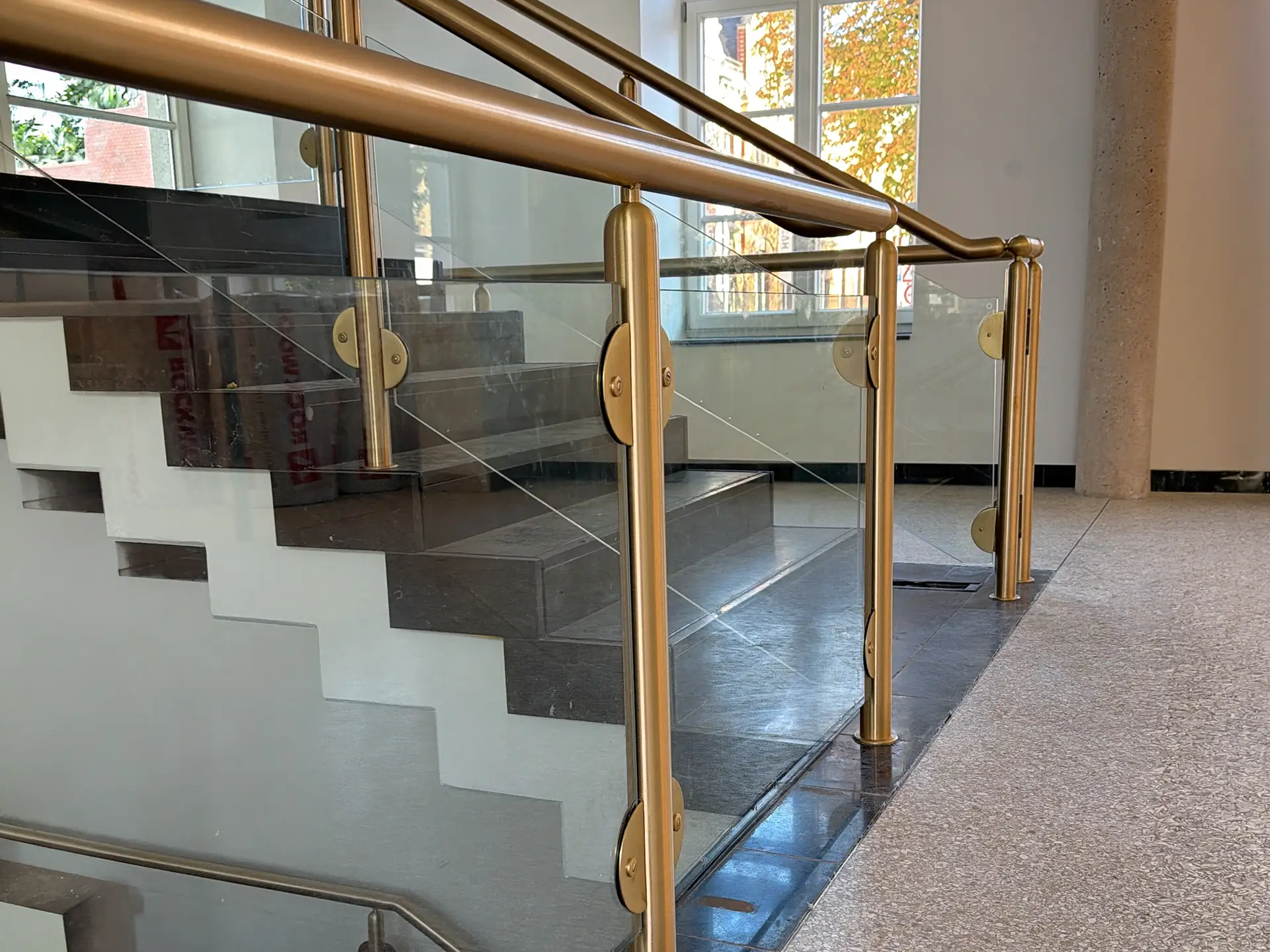 Modernisiertes Treppenhaus im historischen Rathaus Stolberg mit Glasgeländer und goldfarbenen Handläufen.