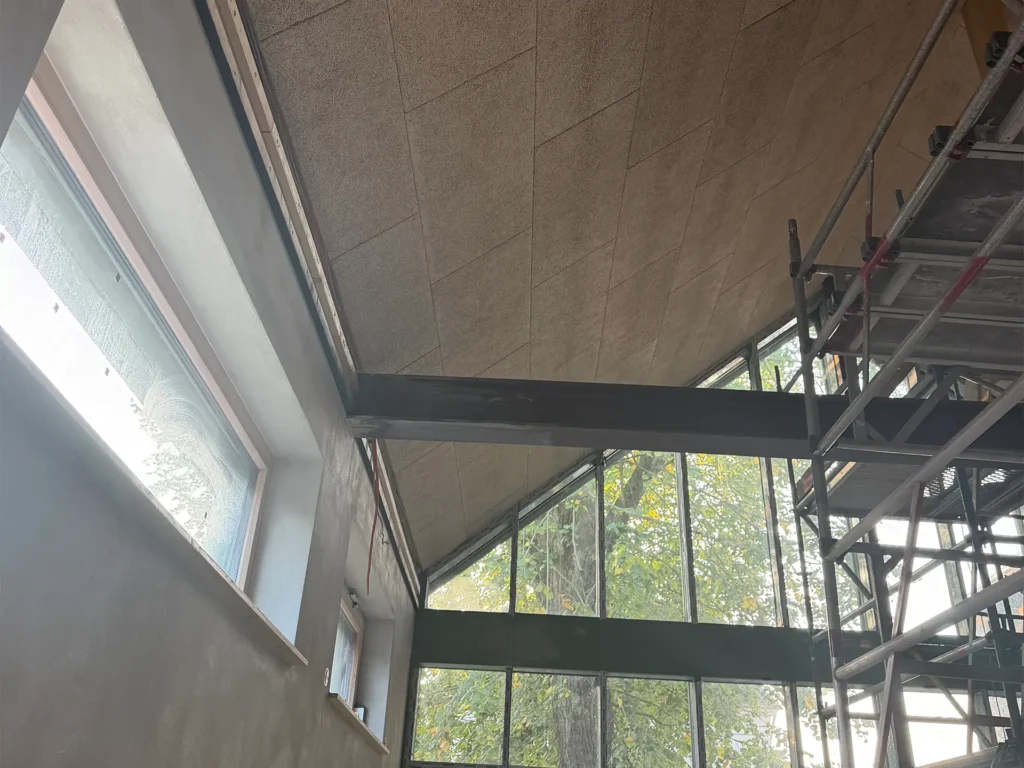 Hoher Innenraum der Kita Vicht mit großer Fensterfront, sichtbaren Deckenträgern und Baugerüst während der Sanierung.