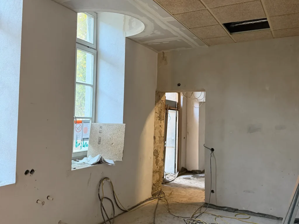 Innenraum der Kita Vicht während des Wiederaufbaus mit verputzten Wänden, offenen Durchgängen und abgehängter Decke.